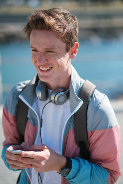 笑，学生和男子与手机和耳机户外移动连接。年轻人，幸福和模糊的背景，一个男人拿着手机进行社交媒体和文本网络图片下载