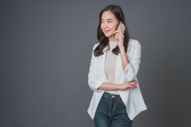 快乐的亚洲女商人使用手机孤立的灰色背景。一名女子在广告媒体中使用智能手机进行交流。图片下载