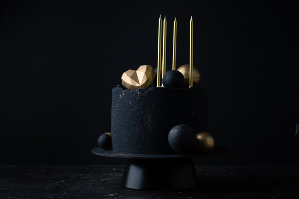 豪华周年蛋糕，黑色天鹅绒喷涂涂层装饰金色巧克力球，心形和蜡烛在顶部。黑色背景为心爱的人准备的复古蛋糕图片下载