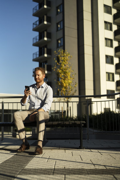 年轻时尚的商人坐在户外的长凳上。图片下载
