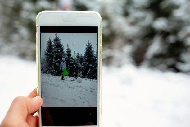 男性手持智能手机，拍孩子们在雪地里玩耍的照片。图片下载