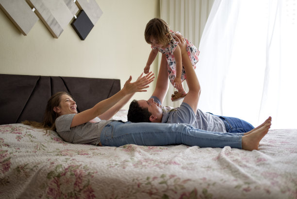 年轻的爸爸妈妈在床上和他们的宝贝女儿玩耍图片下载