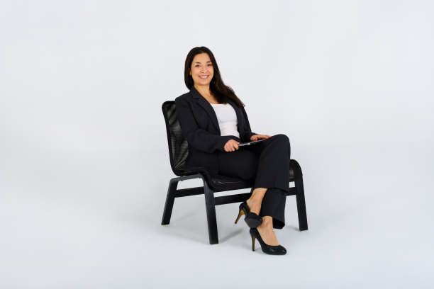 一个自信的商业女性坐在一张黑色的椅子上，看着相机在工作室的照片图片下载