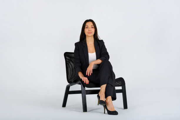 一个自信的商业女性坐在一张黑色的椅子上，自豪地看着相机在工作室的照片图片下载