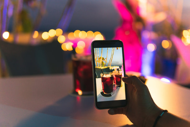 一个不认识的人的手在夜晚露台的桌子上拍了一张清爽的红色饮料的照片，背景是灯光。图片下载