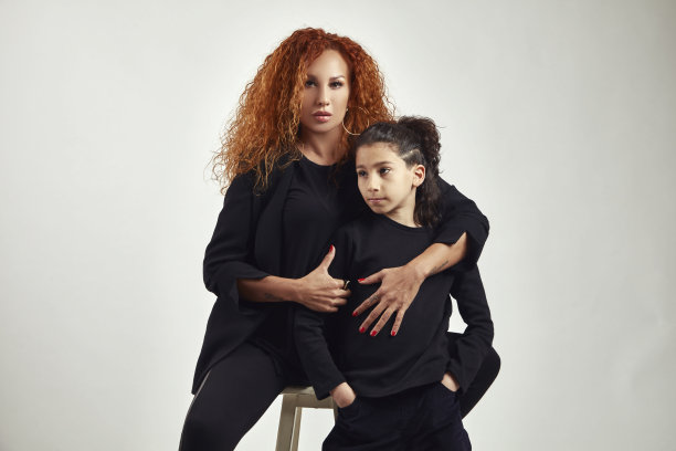 一头卷发的美丽母亲坐在白凳子上，抱着儿子，对着镜头摆姿势。图片下载