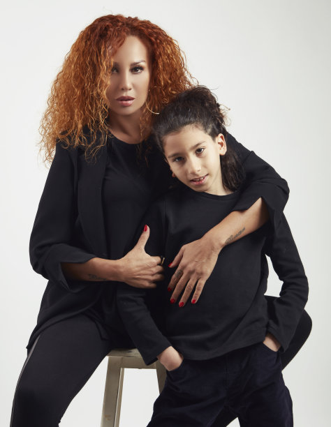 一头卷发的美丽母亲坐在白凳子上，抱着儿子，对着镜头摆姿势。图片下载