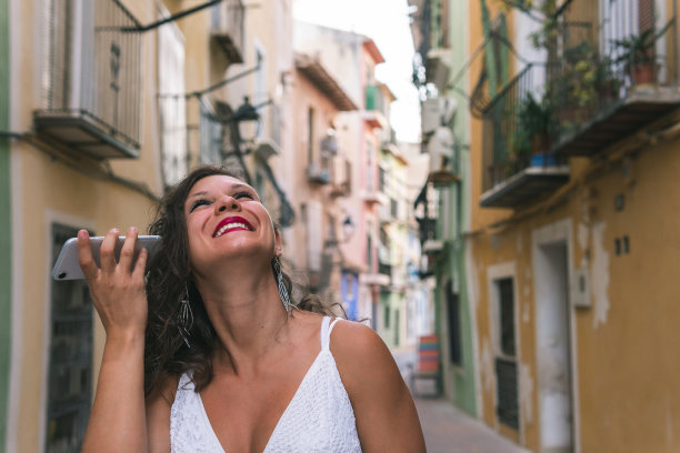 在西班牙阿利坎特市的维拉约奥萨市，一名黑发女子走在色彩缤纷的街道上，一边笑着一边把手机放在耳边听语音信息。图片下载