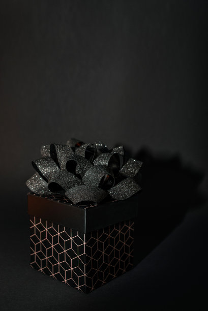 一个黑色的礼品盒，上面有几何图案和黑色背景上的黑色蝴蝶结。度假或打折的极简主义背景图片下载