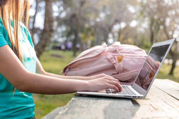 一名面目全非的女大学生坐在公园外，用笔记本电脑学习图片下载