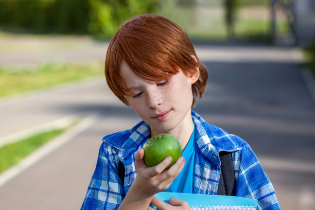 一个可爱的小男孩在户外吃一个绿苹果。为孩子准备的健康学校零食。回到学校的概念。图片下载