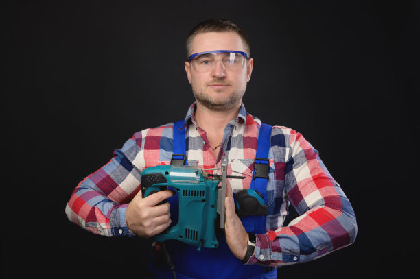 穿着格子衬衫和工装裤的微笑男子在黑色背景上拿着一块拼图，另一只手做着合十礼的手势图片下载