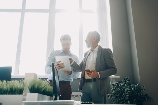 两个自信的男人一边在办公室工作一边讨论业务图片下载