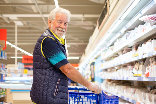 大胡子老人推着购物车在超市里买杂货，小心翼翼地考虑成本——消费主义的概念，价格上涨，通货膨胀图片下载