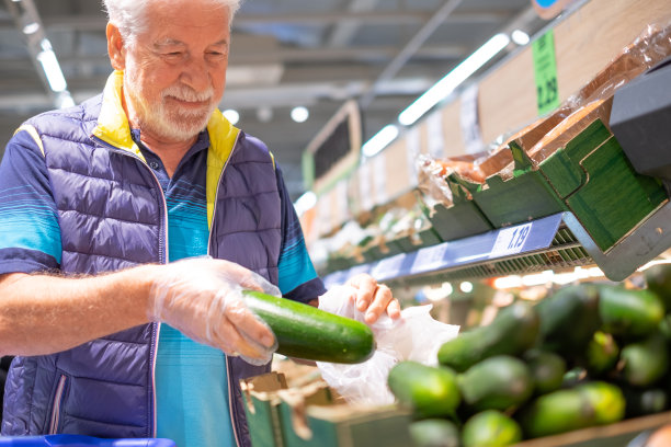白发老人在超市里选购杂货，挑选蔬菜，小心翼翼地考虑成本——消费主义的概念，价格上涨，通货膨胀图片下载