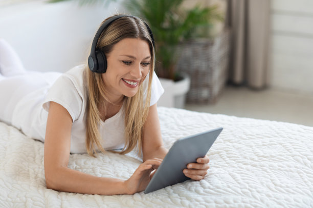 快乐的年轻女子躺在床上垫和耳机图片下载