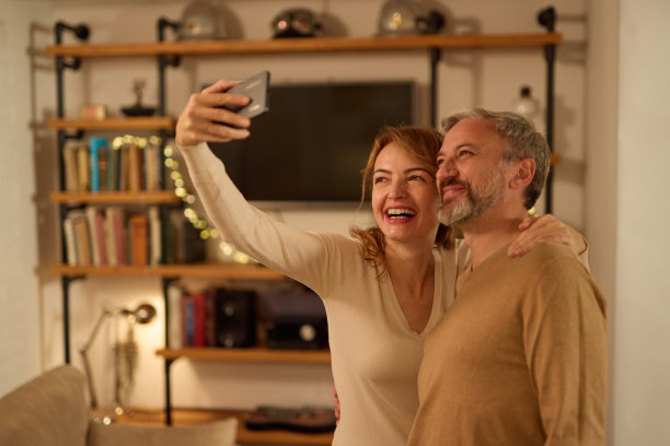 快乐的成熟夫妇在家里用智能手机自拍图片下载