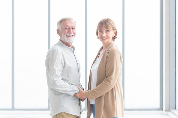 快乐的老夫妻回家了。高级跨种族丈夫和妻子在客厅手牵着手微笑。图片下载