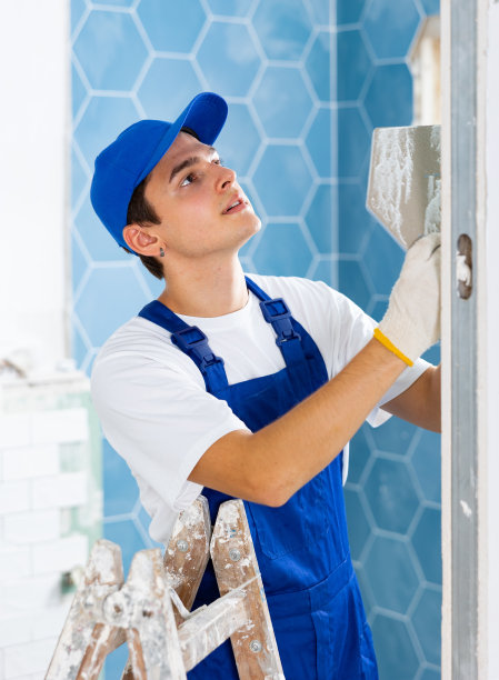 年轻的承包商在室内装修时在墙上贴瓷砖图片下载