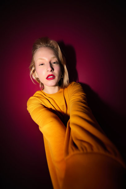 一个严肃的金发女孩把手伸向相机，看着它。洋红色万岁。图片下载