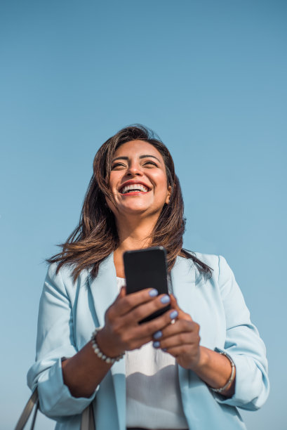垂直形象的商业女性与手机和微笑。快乐的拉丁女人在户外出勤。本空间图片下载