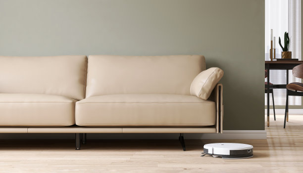 白色现代吸尘器机器人在工作，吸尘，清洁客厅的木地板，米黄色真皮沙发在鼠草绿色的墙壁上图片下载