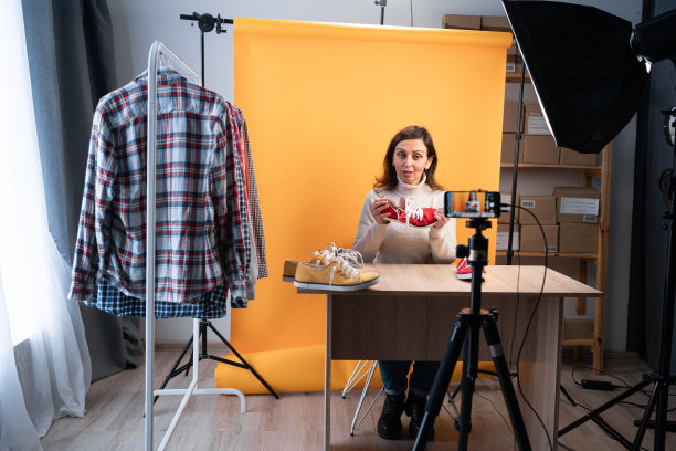 社交媒体影响者评论运动鞋。一名女子在视频上发布关于男性运动鞋的视频，用智能手机摄像头在家庭工作室拍摄自己。图片下载