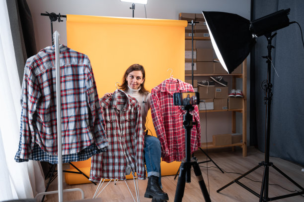 美女博主在她的商店里录制vlog视频和直播时，在智能手机摄像头前展示衣服。商务在线电子商务在家里图片下载