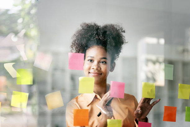 年轻的笑脸迷人，女商人用便利贴在玻璃墙上写战略商业计划发展成长成功图片下载