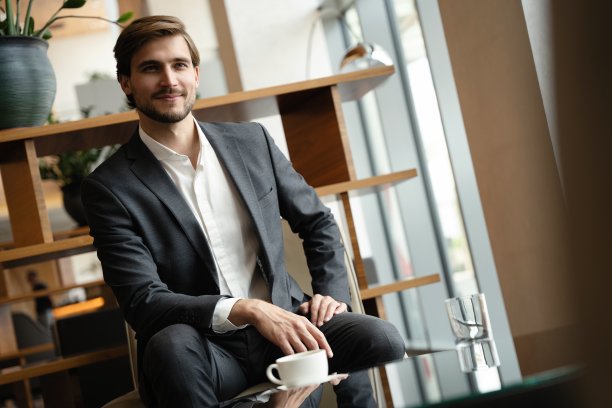 图为中年帅气商人，身着黑色正装，坐在酒店大堂扶手椅上。图片下载