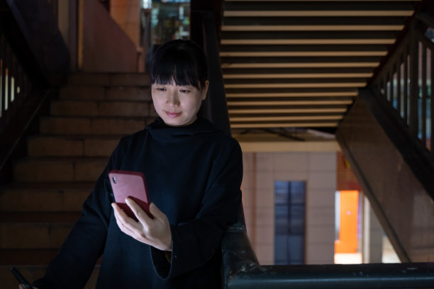 晚上，一个女人站在走廊上用她的手机图片下载