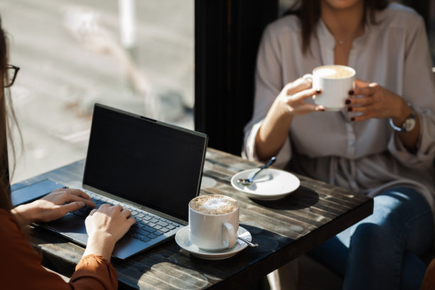 两个年轻的女商人在咖啡馆里一对一地开会。下班后的朋友们在阳光明媚的日子里闲聊，坐在靠窗的桌子上喝咖啡。图片下载
