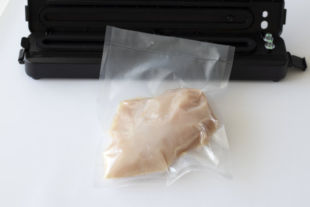 真空机旁白色背景的吸尘鸡胸。准备用真空技术烹饪图片下载