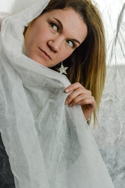 一个美丽的金发女人的肖像，谁是隐藏在白色织物后面，看着一边图片下载