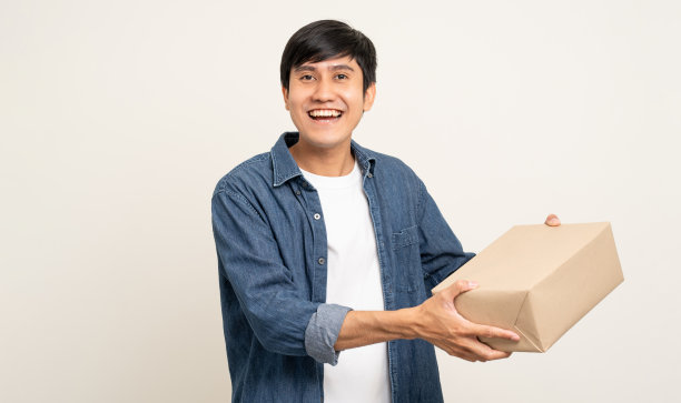 年轻兴奋的亚洲男子与许多包裹纸板站在孤立的白色背景。快乐的男子拿着许多包裹盒子从快递服务收到图片下载