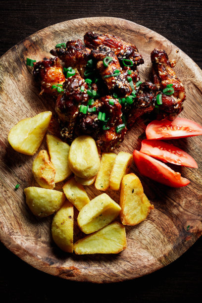 烤鸡翅加芝麻和大葱，放在木盘上加土豆和西红柿图片下载