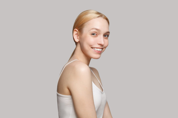 金发女子在白色顶部微笑孤立的灰色背景。美容、化妆品、护肤、魅力图片下载