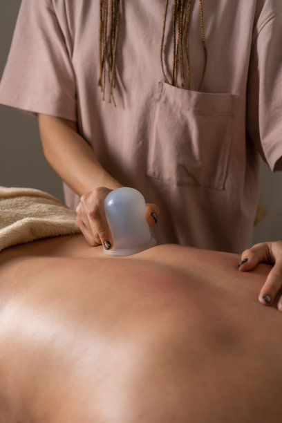 特写的按摩师做背部按摩使用硅胶真空罐。拔火罐治疗一位年轻女性的背部疼痛。健康理念，呵护身体。垂直图图片下载