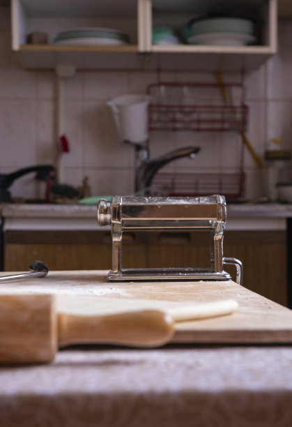 近距离滚动意大利面面团的机器。将面团擀成薄层的自动化过程。做意大利面条是一种乐趣。意大利菜。我们在家做饭。真正的厨房图片下载