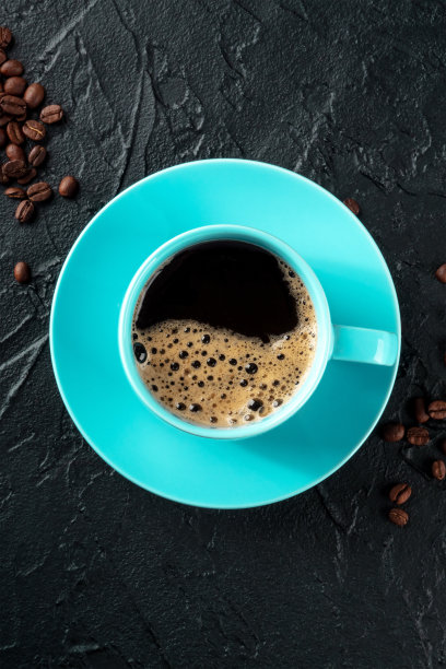 蓝绿色咖啡杯和咖啡豆，顶部拍摄在黑色背景上图片下载