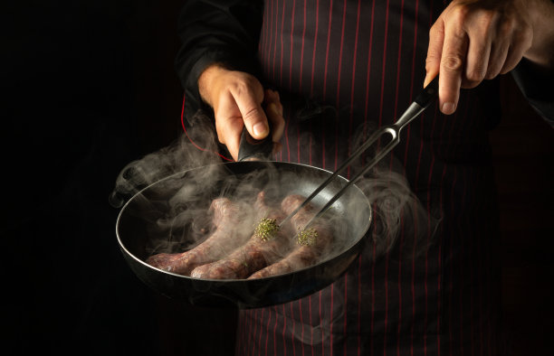 专业厨师在热锅里用蒸汽煎肉肠。黑色背景的酒店菜单或食谱。图片下载