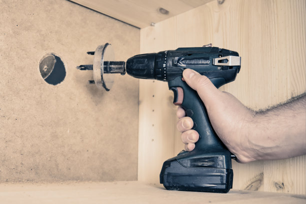 在钻头上钻圆孔的。用电动螺丝刀上带喷嘴的圆锯锯家具图片下载