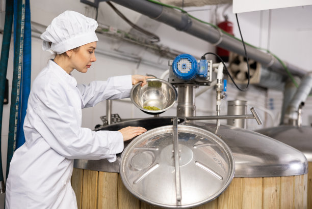 女酿酒师将啤酒花颗粒从碗中倒入发酵罐图片下载