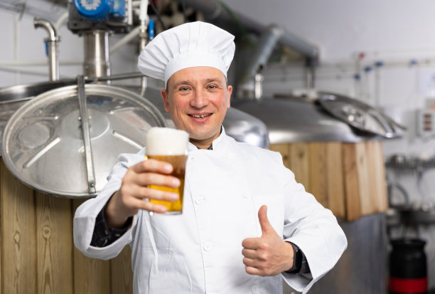 快乐的啤酒酿造者举起一杯啤酒，竖起大拇指图片下载