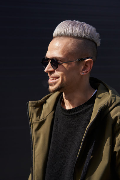 戴着墨镜的白头发青年，身穿白色上衣和绿色夹克，笑容满面地站在那里图片下载