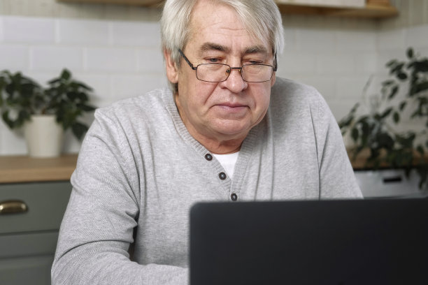 戴眼镜的高级男性企业主坐在笔记本电脑前的办公桌前。在家工作的成功年长男性。灰色的头发60 - 70岁的老忙人打字键盘看显示器。距离办公室图片下载
