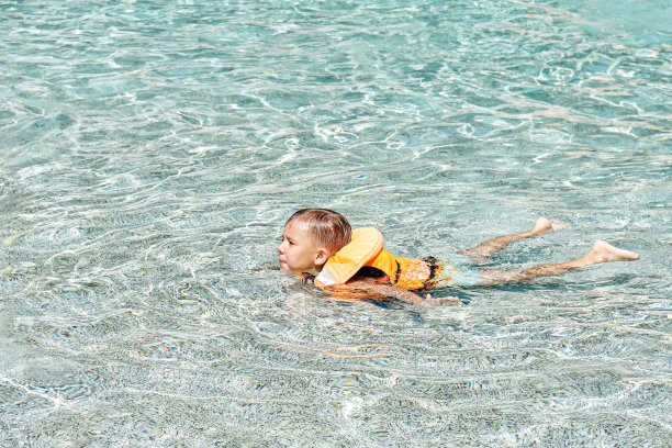穿着救生衣放松的学龄前儿童在游泳池学习游泳图片下载