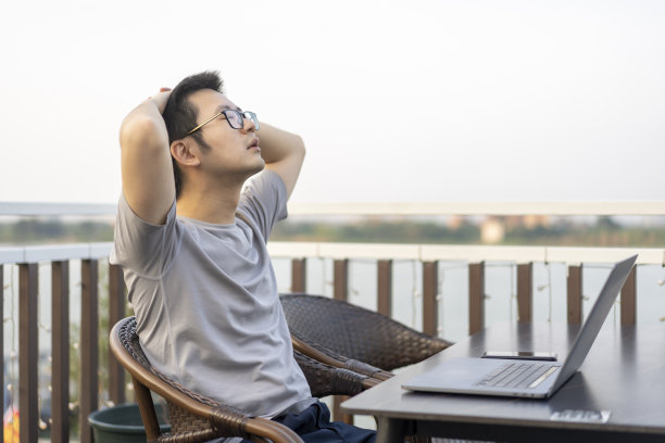 一名亚洲男性自由职业者在河边的露天咖啡馆使用笔记本电脑时感到疲惫图片下载