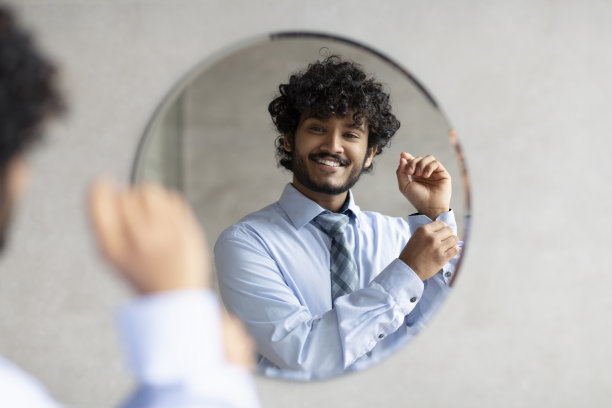 快乐的大胡子印度商人站在浴室的镜子前，扣上衬衫图片下载