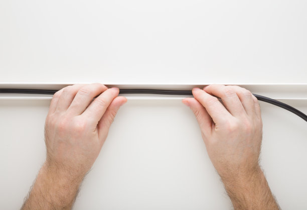 年轻的成年男子双手将黑色的新电线放在白色背景的塑料通道中。特写镜头。视角镜头。电工工作。自顶向下视图。图片下载